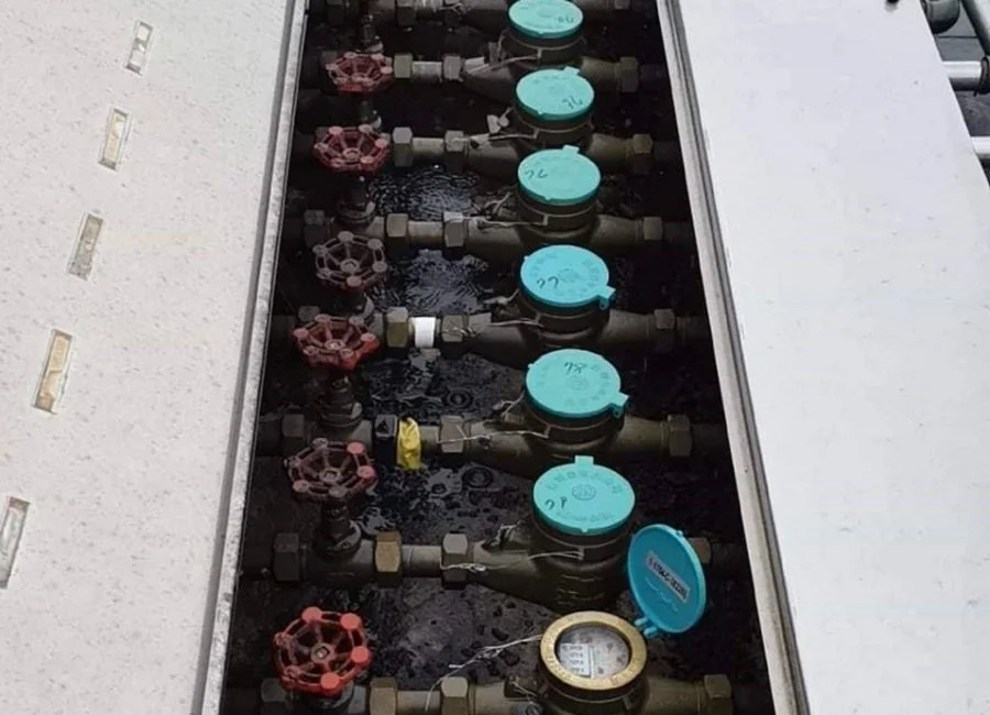 Multiple water meters and valves installed in a utility box, with some covers open, showing the meters and pipes inside.