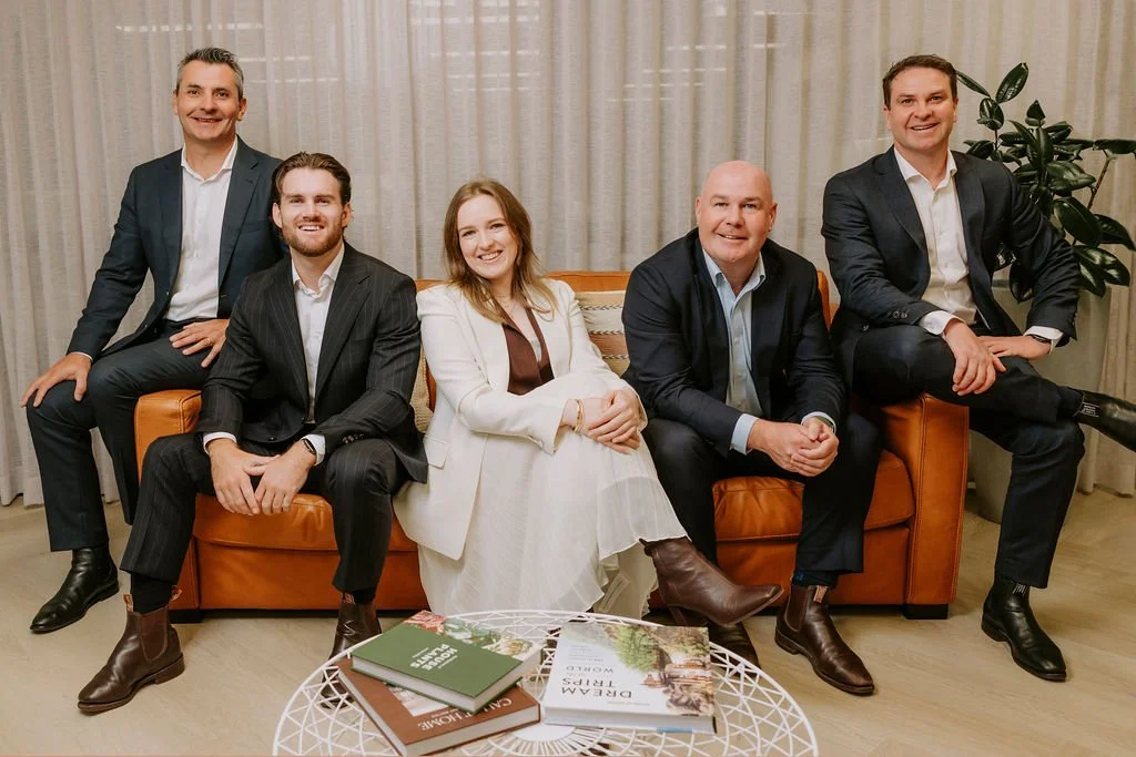 Up Wealth Management wealth management NSW South Coast team in formal attire sitting and standing on a leather sofa in a living room with curtains.