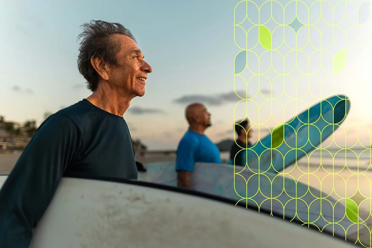 Three men stand with surfboards on the beach at sunset, smiling as they look out over the ocean.