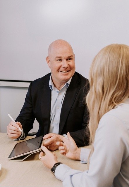 Aaron Hopkins Director & Financial Adviser Up Wealth financial advisor for business owners and woman having a conversation at a meeting table at Up Wealth Management office, smiling and holding a stylus, and the woman using a tablet.