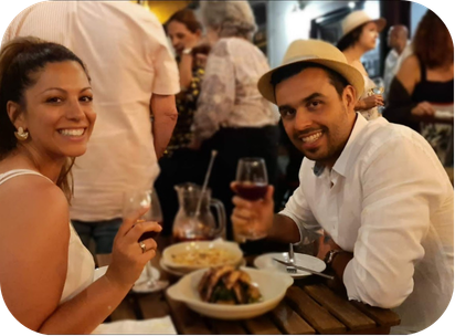 A man and woman enjoying drinks and food at a restaurant with other people in the background.