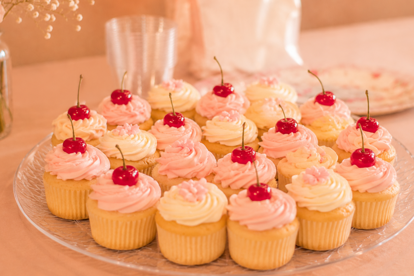 A tray of cupcakes decorated with pink frosting and topped with cherries.