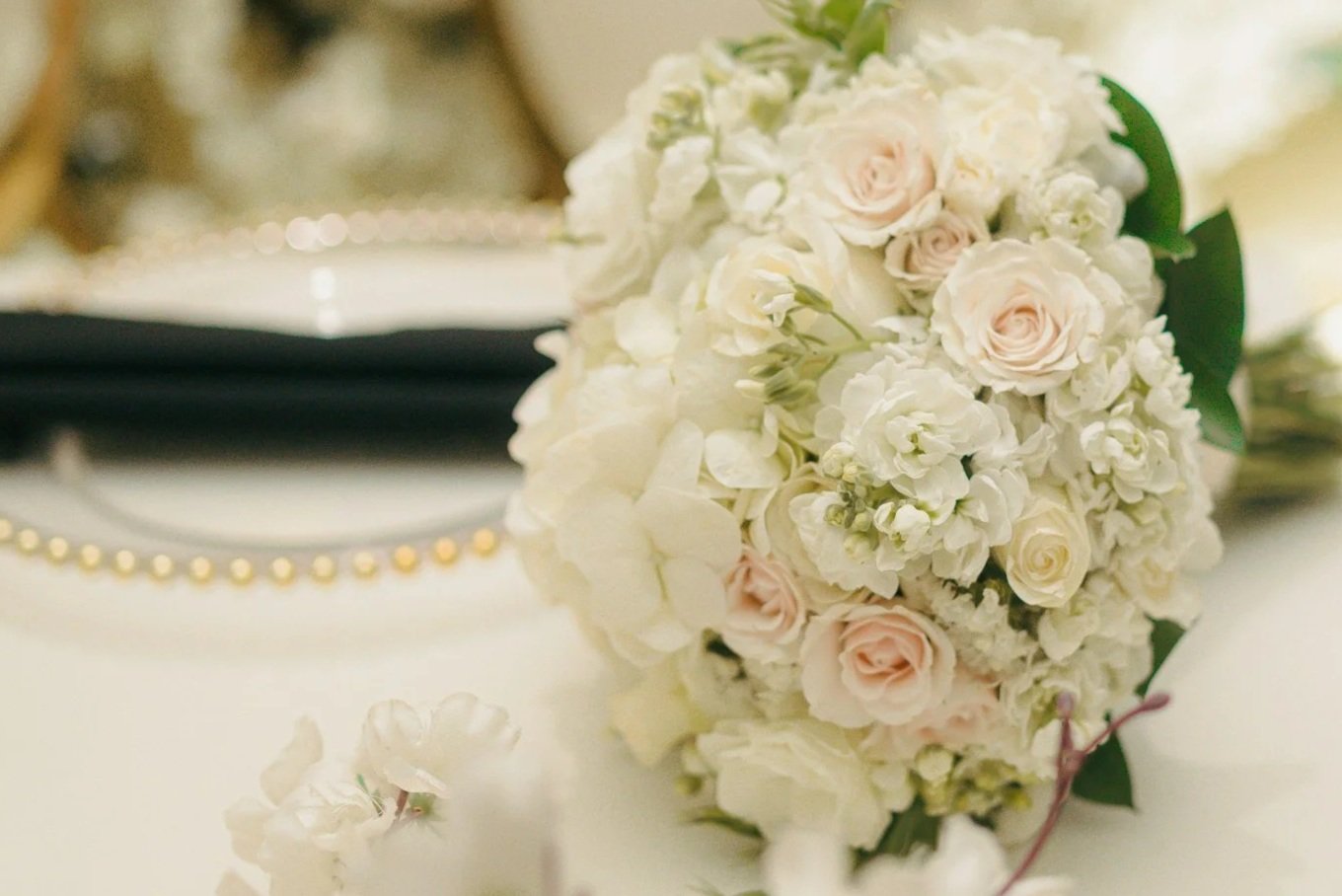 A bouquet of white and pale pink roses and hydrangeas on a white surface.