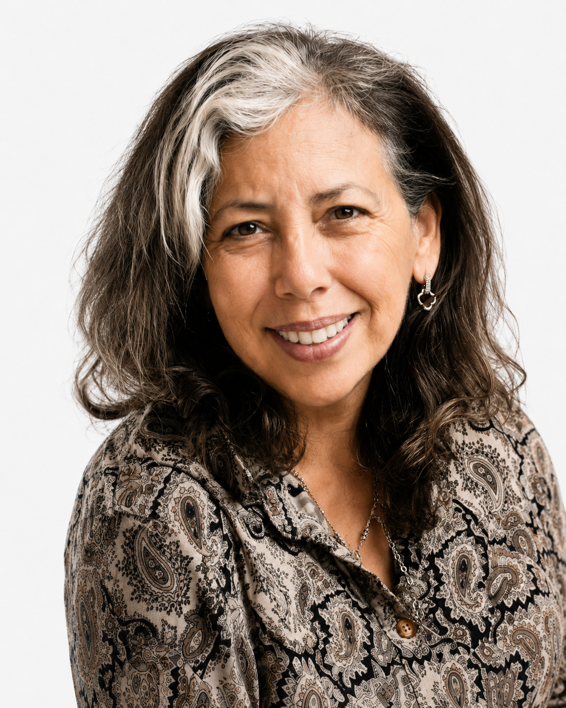 A smiling middle-aged woman with long, wavy hair, black and gray, wearing earrings and a patterned blouse, against a plain white background.