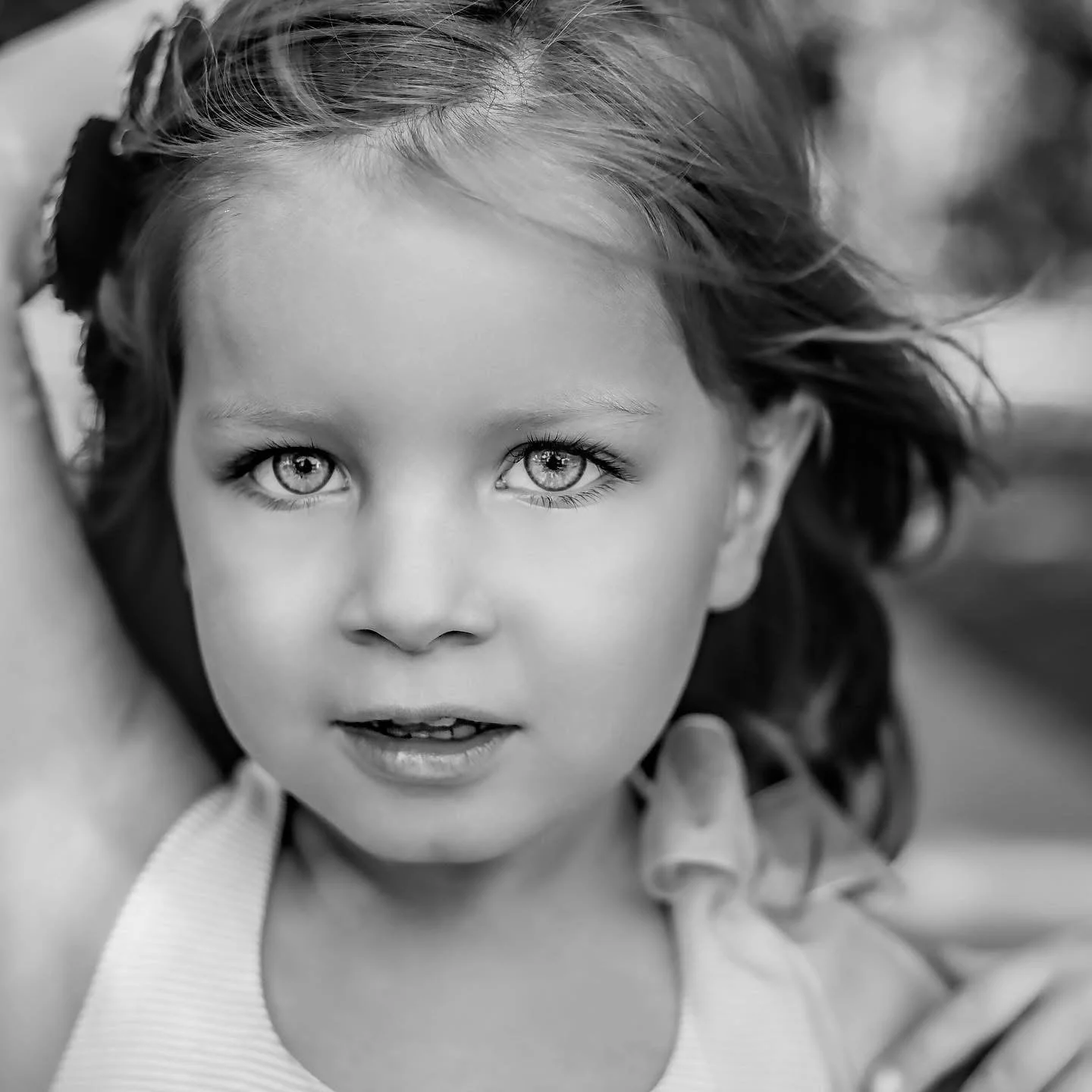 Close-up black and white photo of a young girl with curly hair and bright eyes, looking directly at the camera.