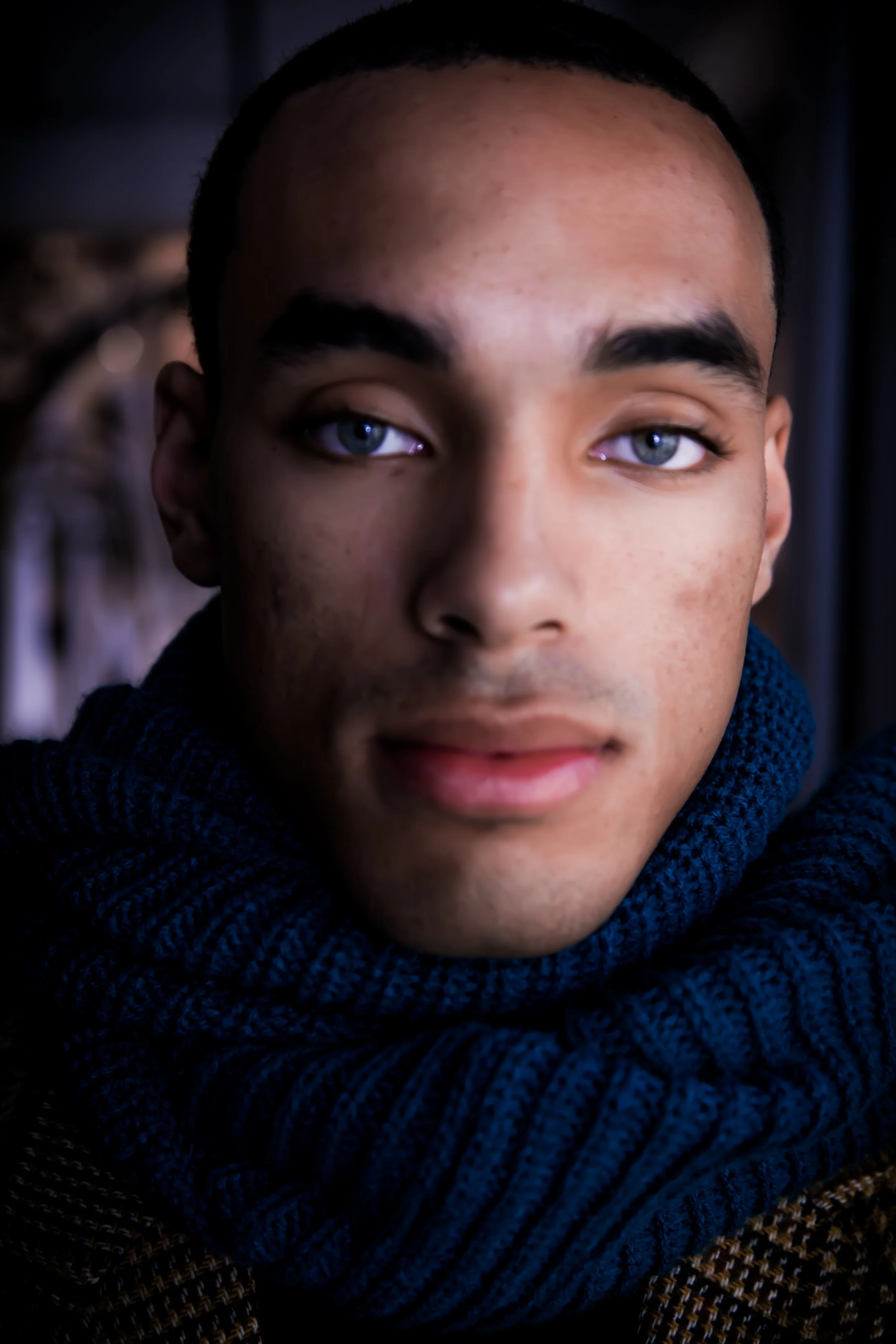 Close-up of a person's face, showing blue eyes, dark eyebrows, and a dark blue knitted scarf.