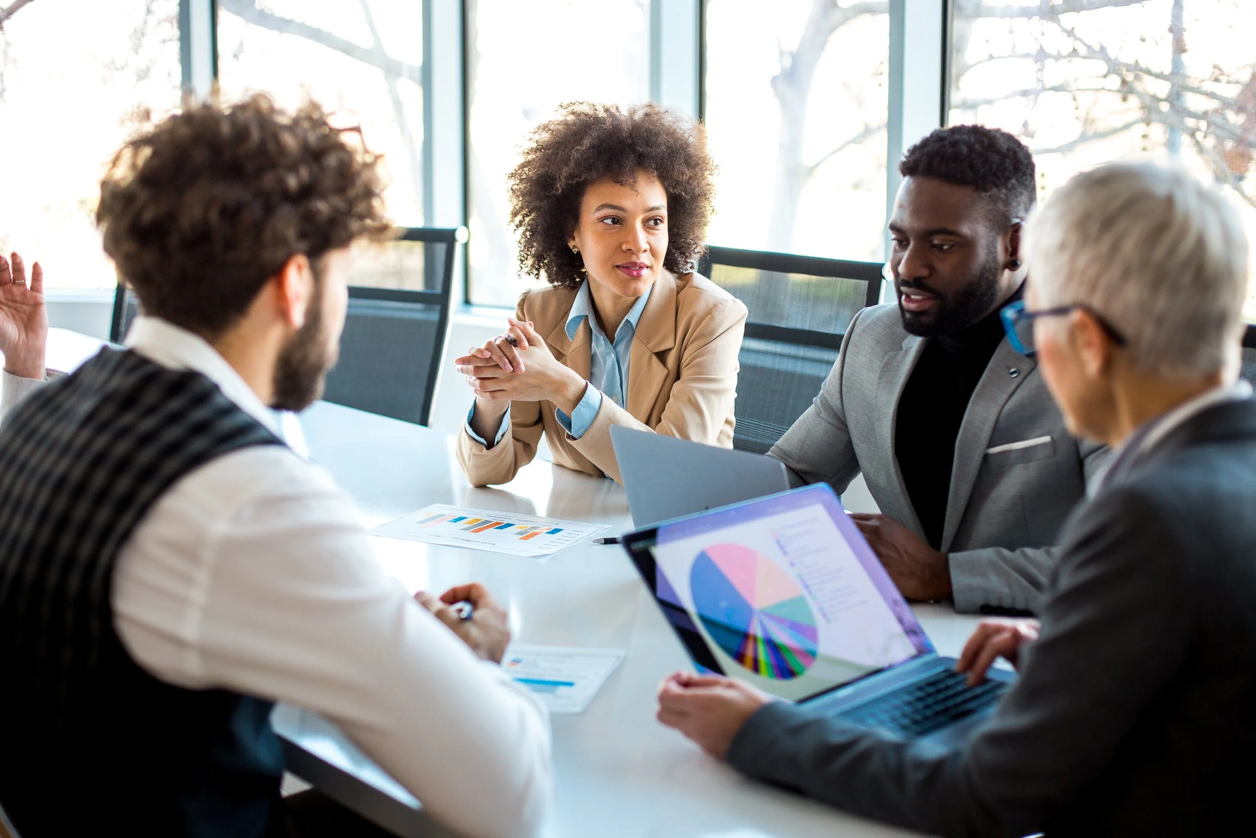 Group of diverse professionals engaged in a business meeting in a conference room with large windows.