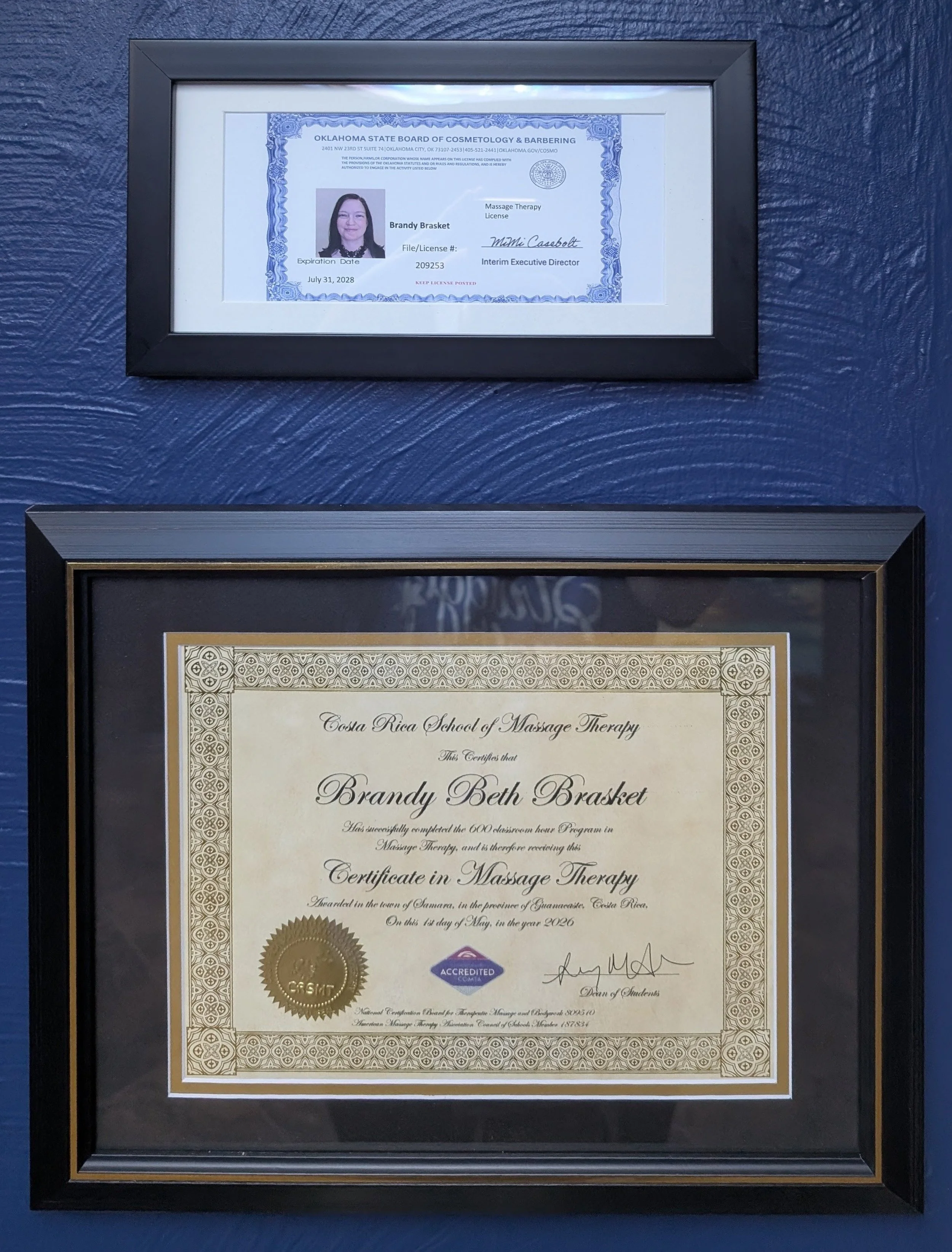 Framed certificate and diploma on a blue wall, awarded to Brandy Beth Brasket for completing massage therapy program, featuring official seals, signatures, and decorative borders.