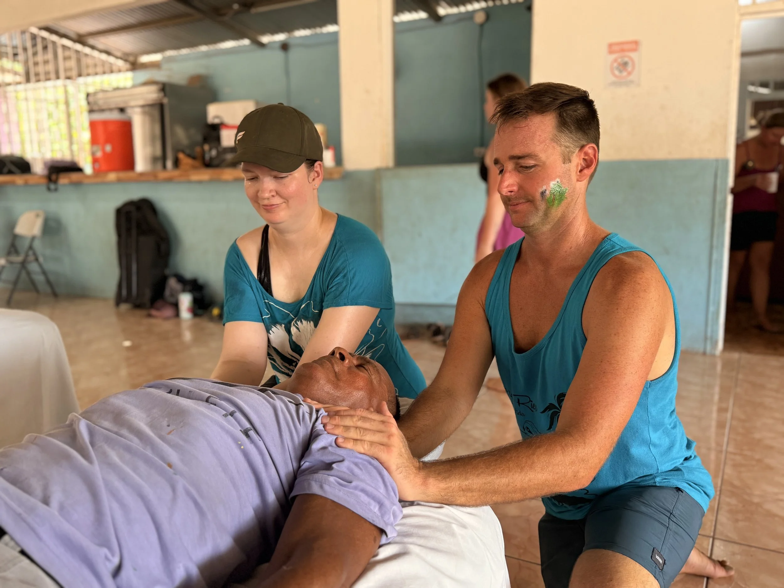 Image of Brandy and another massage therapist providing massage to a person at a community event, in Samara, Costa Rica.