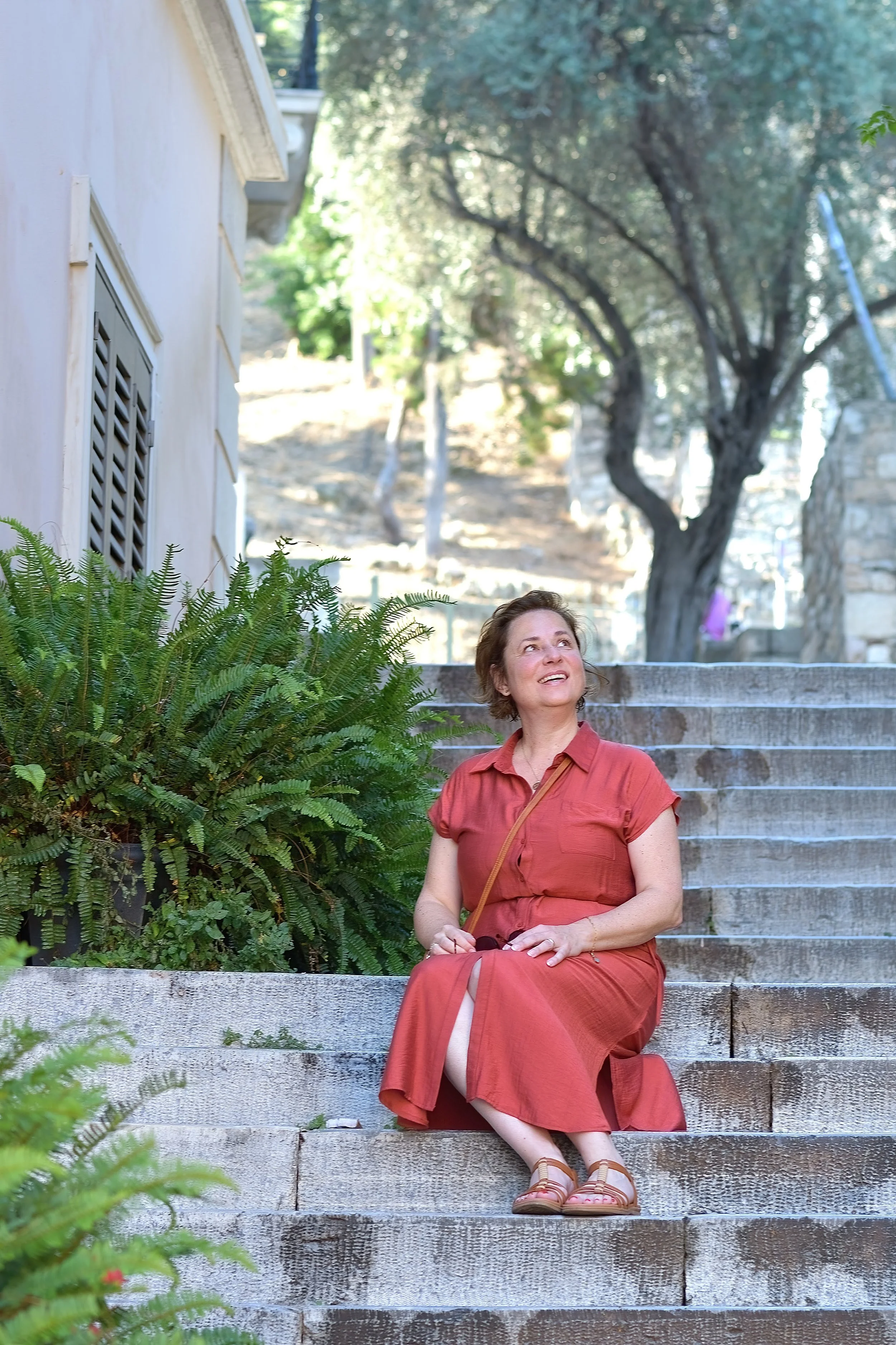 Marcela Kratochvilova sitting on stone steps in a rust dress, looking upward thoughtfully