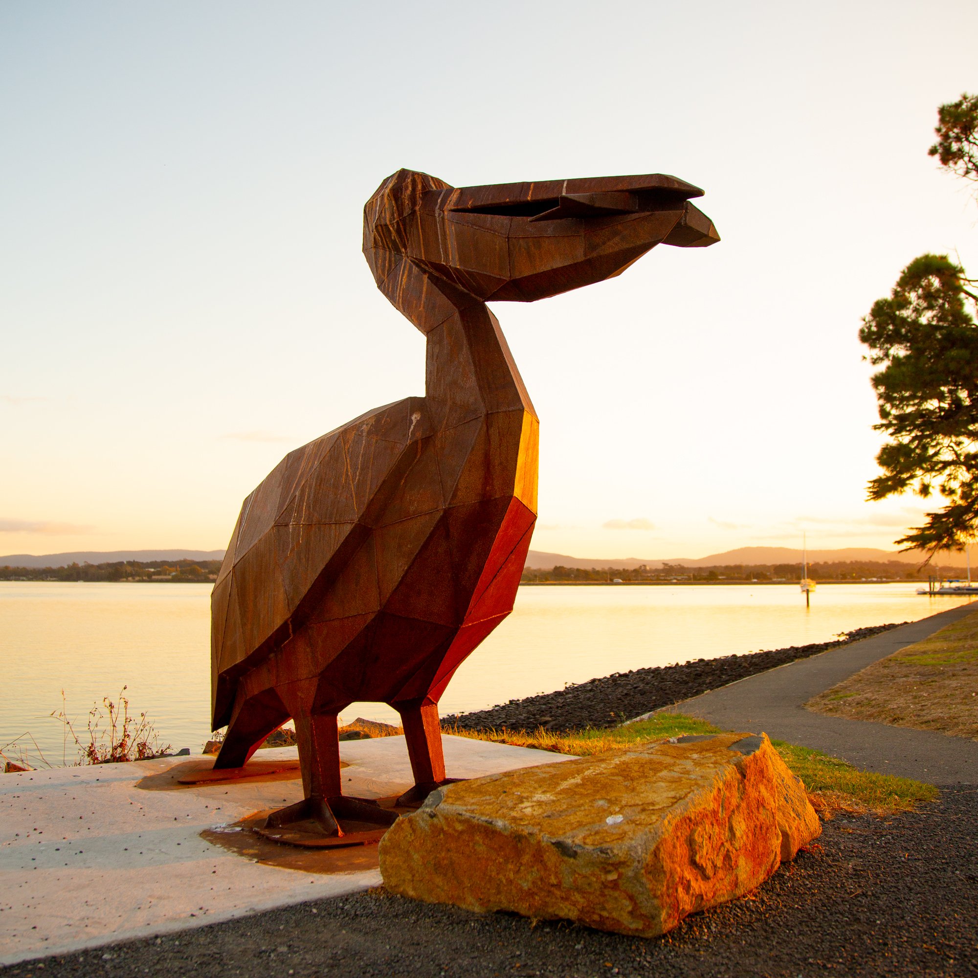 low poly corten steel pelican with fish in beak at sunset in georgetown tasmania