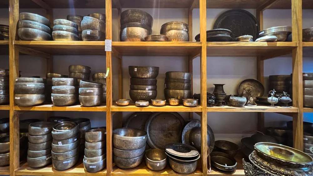 Wooden shelves filled with various sizes of antique metal bowls, containers, and decorative items.