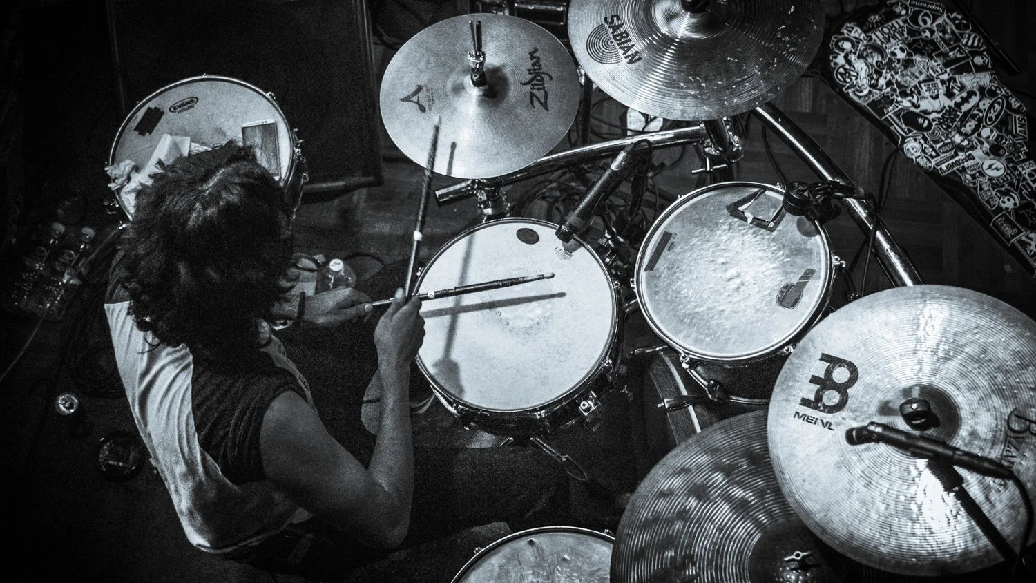 Black and white photo of a drummer playing a drum set, viewed from above. The drum set includes cymbals and drums, with a person holding drumsticks.