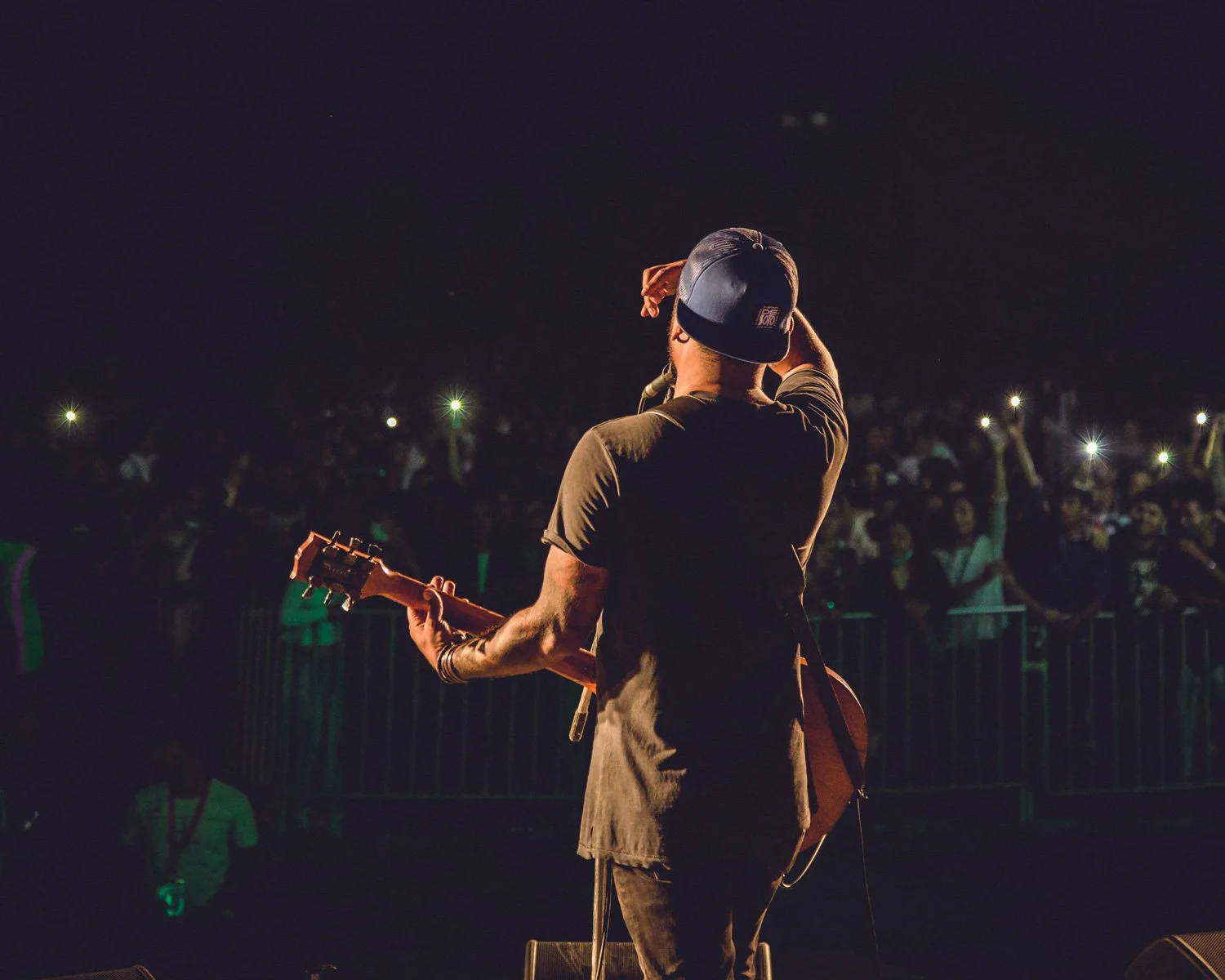 Musician on stage playing guitar at night with an audience holding lights in the background.