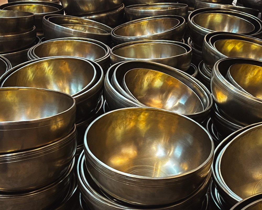 Stacks of shiny, metallic singing bowls arranged in multiple rows.