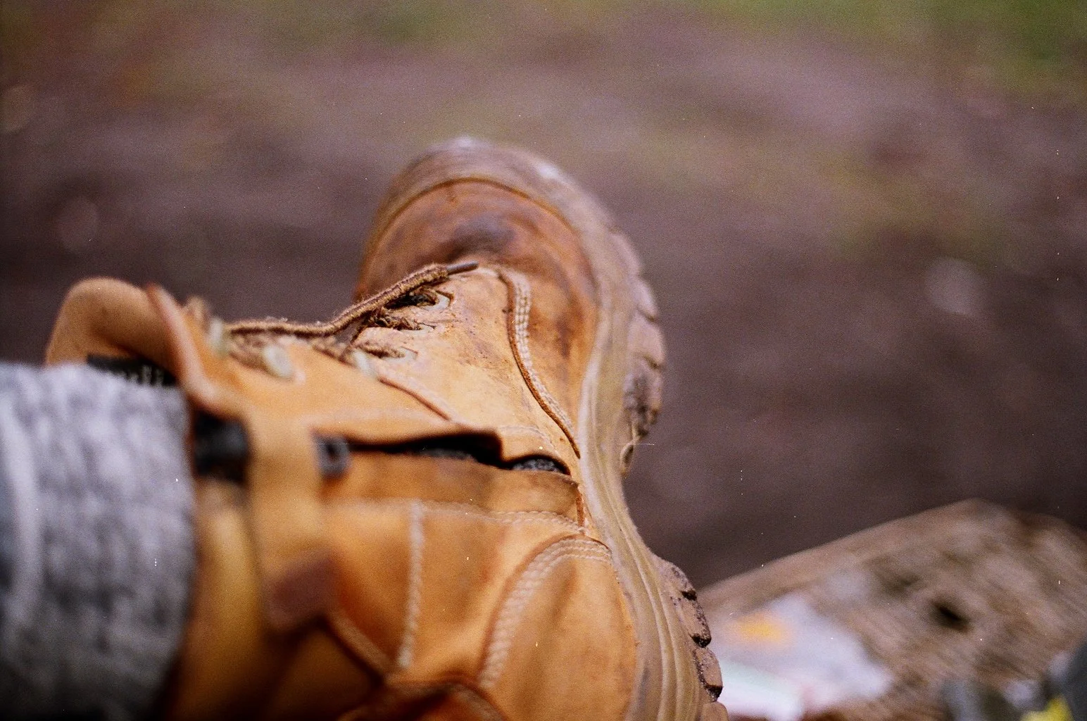 Close-up of a brown hiking boot laced up, resting on a rough wooden surface outdoors with blurred background.