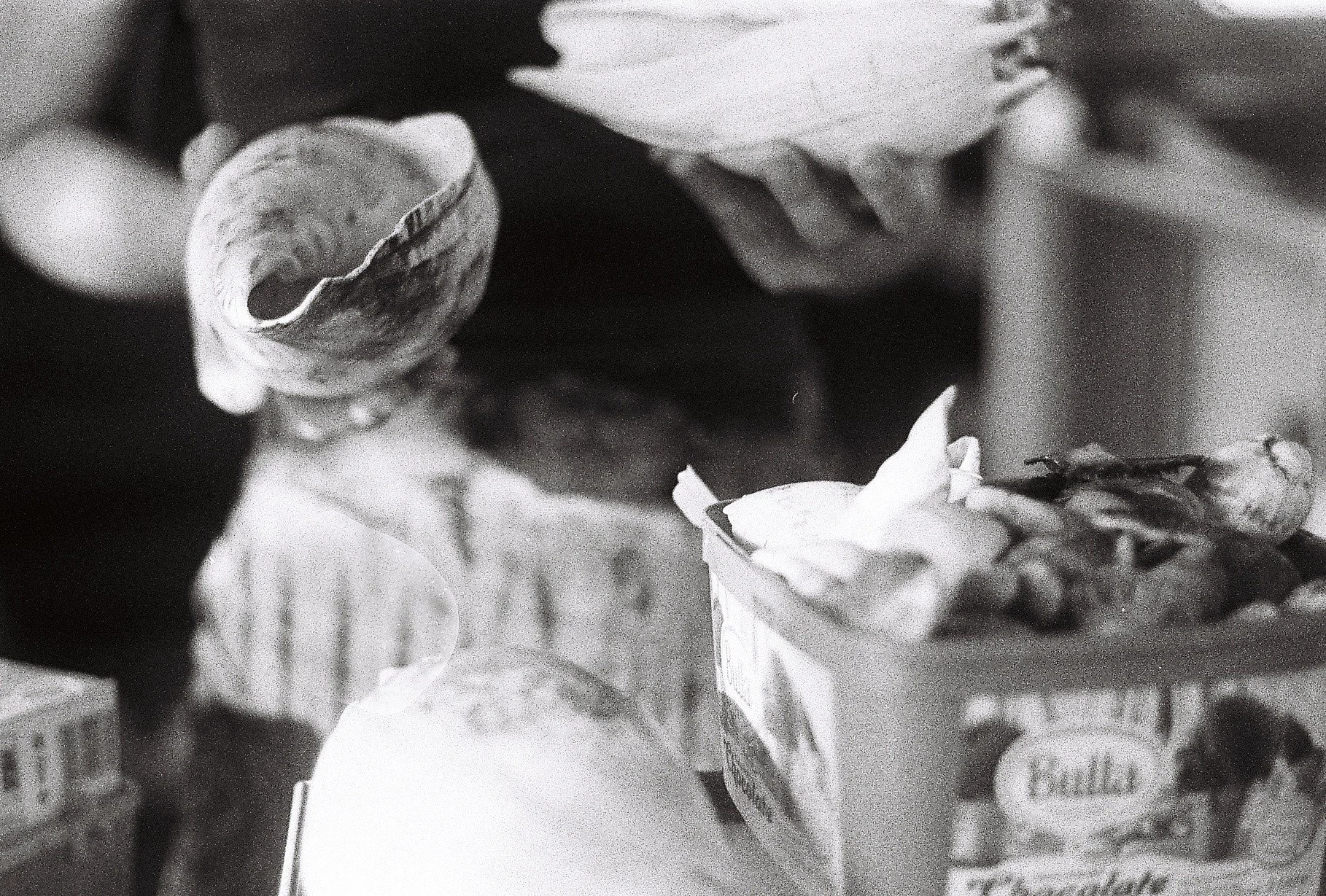 A black and white photo of various snack and food items, including a box of crackers, a nut or snack mix container, and a broken cupcake.