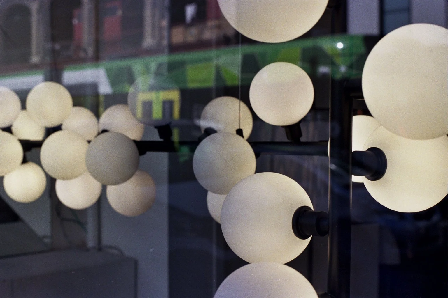 Close-up view of modern spherical white light fixtures mounted on a black structure, reflected in a glass surface.