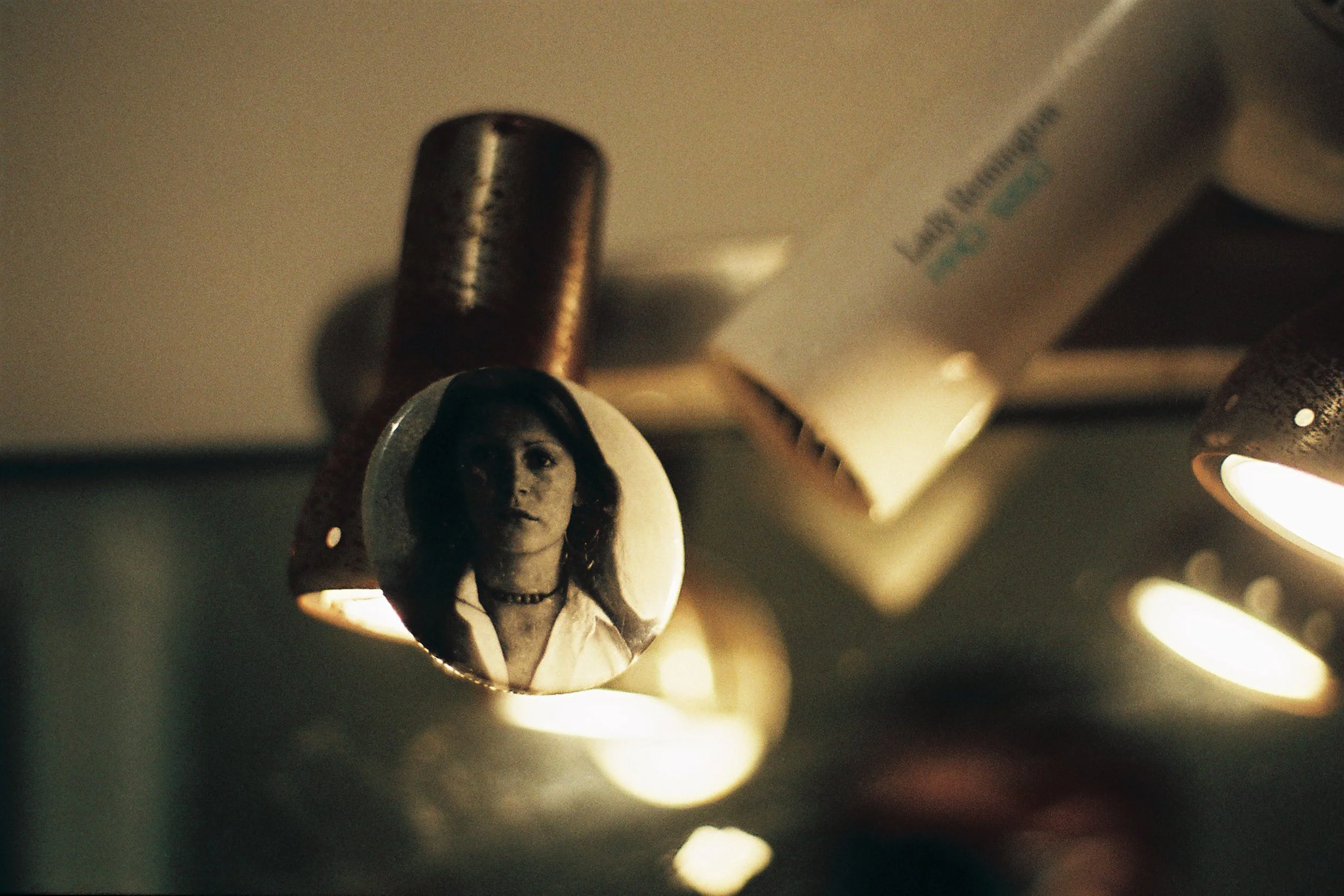 Close-up of a lipstick with a custom mold of a woman's face on the top, featuring dark hair, a choker, and expressive eyes.