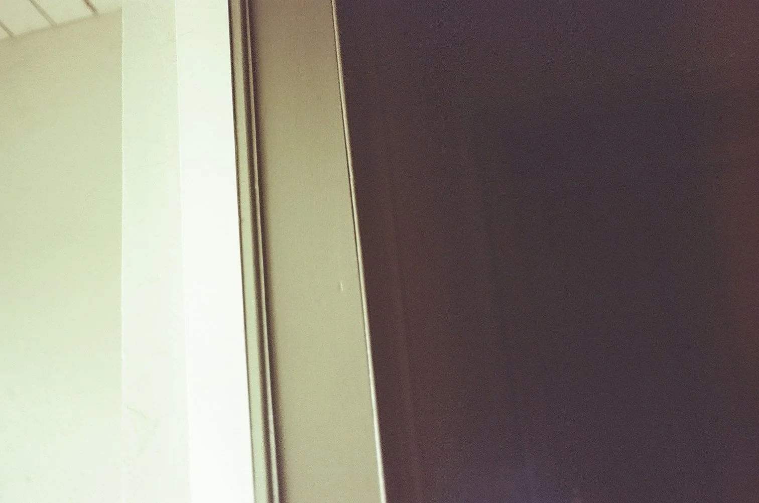 Part of a doorway with a light-colored wall on the left and a dark-colored door on the right, viewed from a close angle.