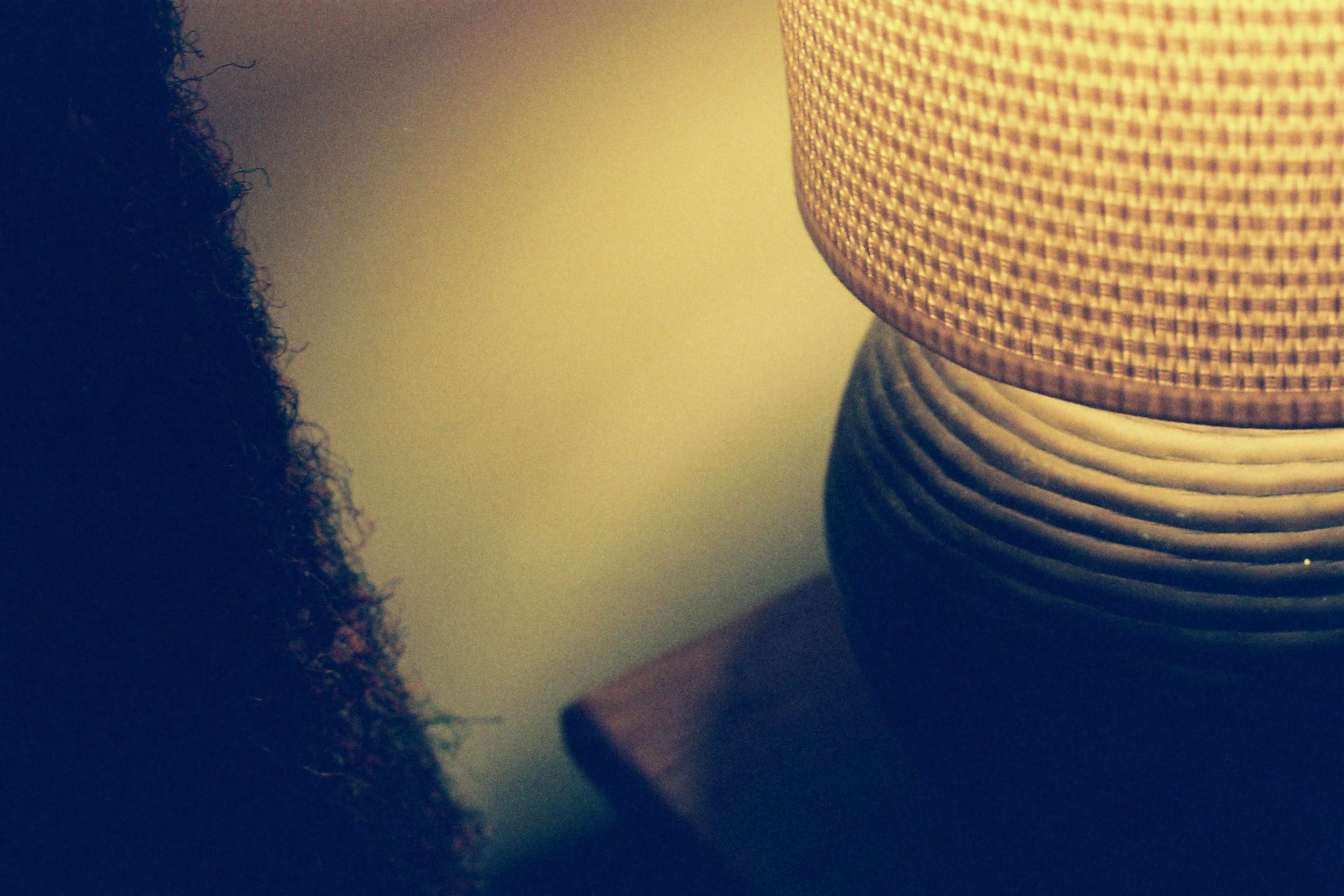 Close-up of a beige woven lampshade with a textured pattern, accompanied by a ribbed metallic base, placed on a surface with a blurred background.