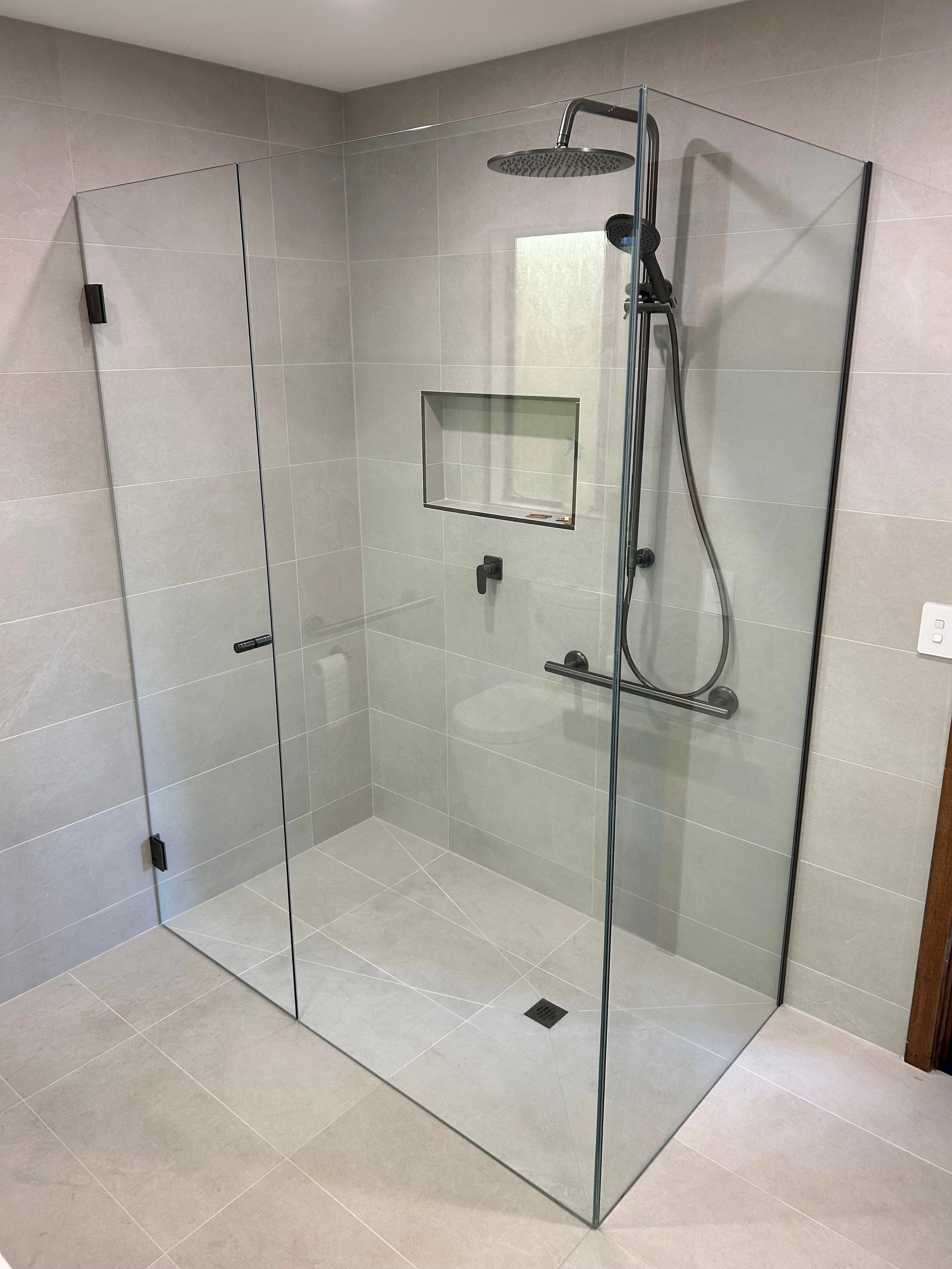 Modern walk-in shower with glass walls, rain showerhead, handheld shower, recessed niche, and neutral tile decor.
