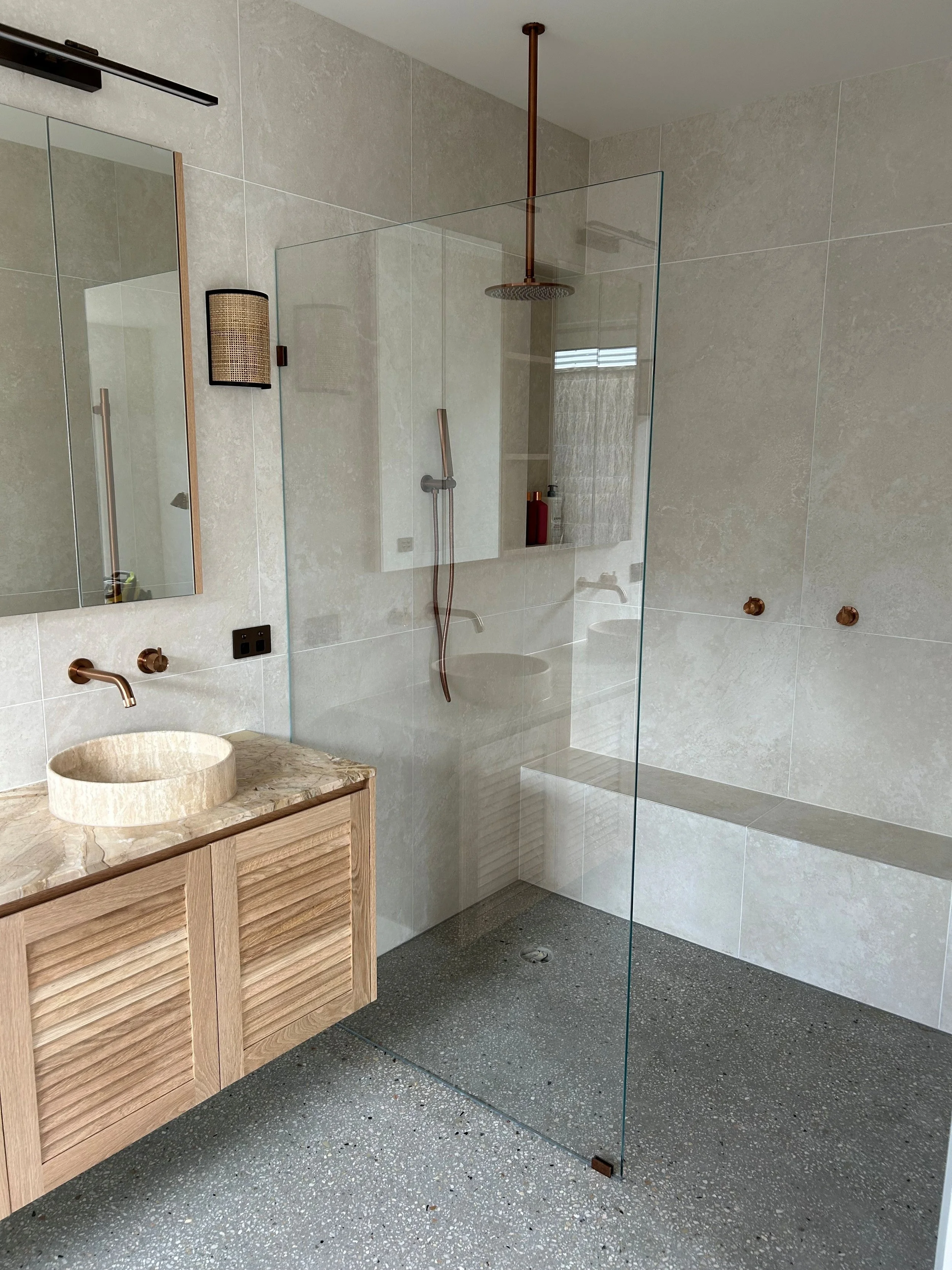 Modern bathroom with wood vanity, marble sink, glass shower partition, beige tiled walls, and a humidifier attached to the shower wall.