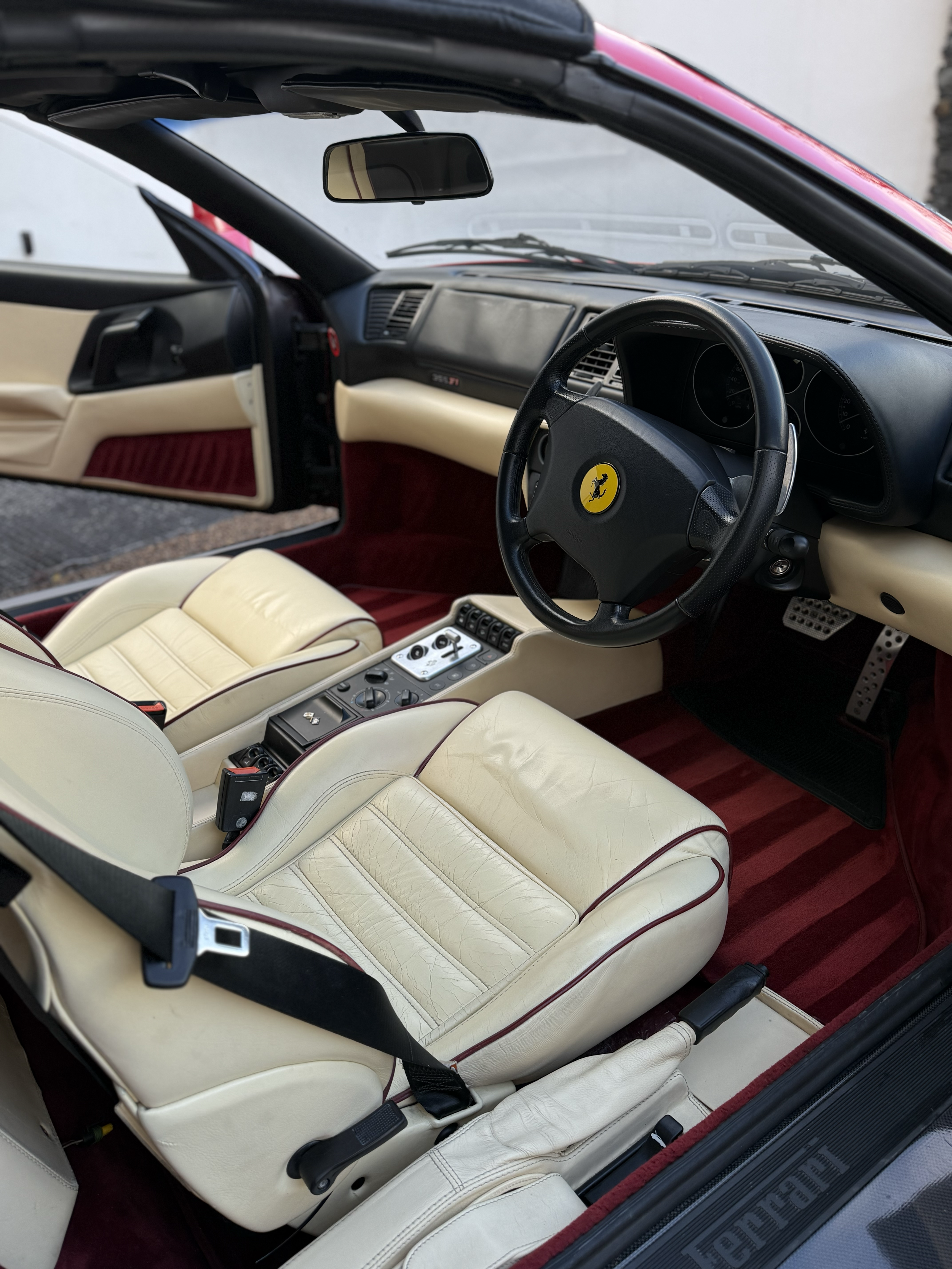 The interior of a Ferrari sports car, showcasing beige leather seats, a black steering wheel with the Ferrari logo, and a dashboard with various controls.
