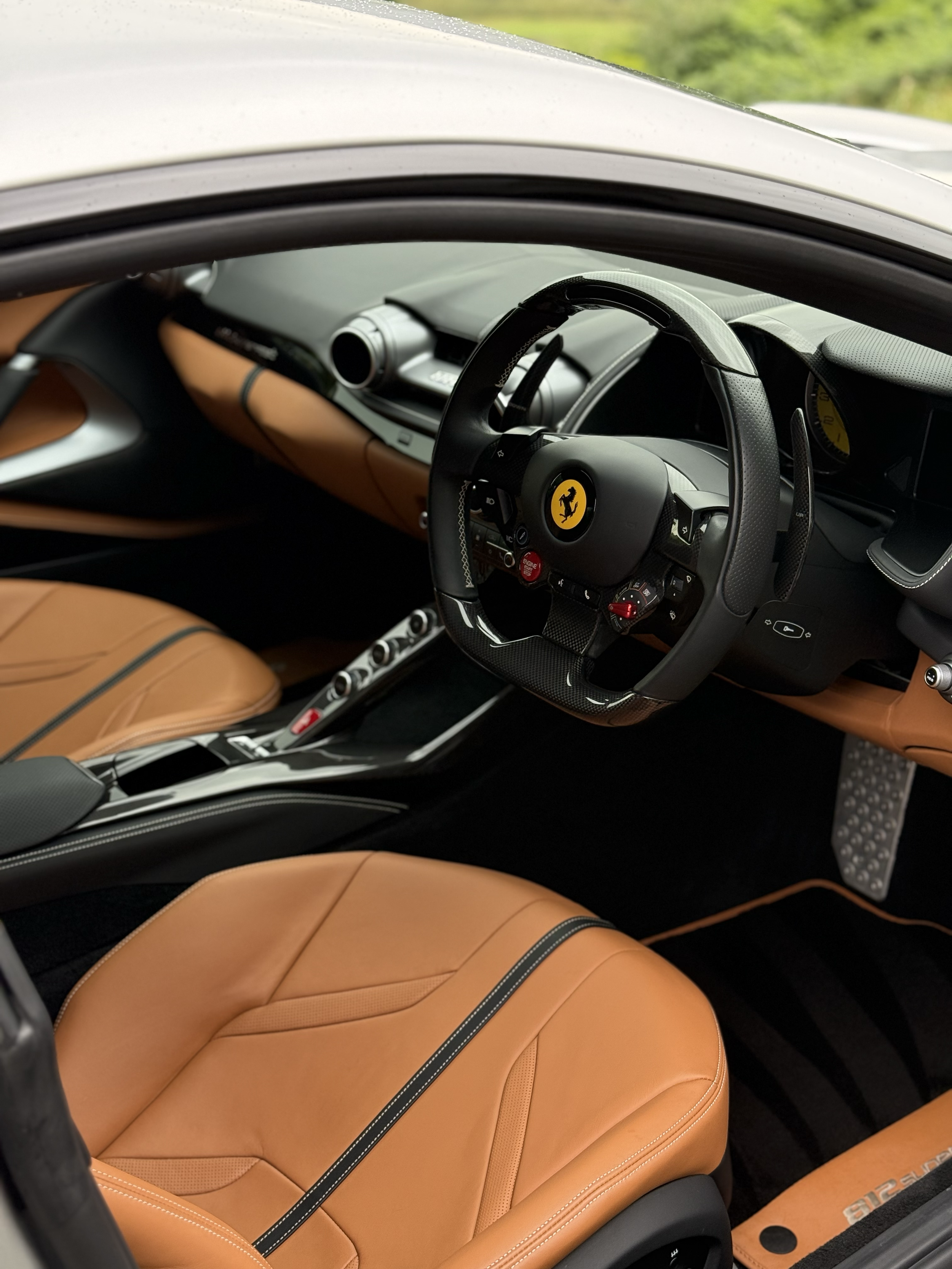 The interior of a luxury sports car with tan leather seats, a black steering wheel with a Ferrari emblem, and a modern dashboard.