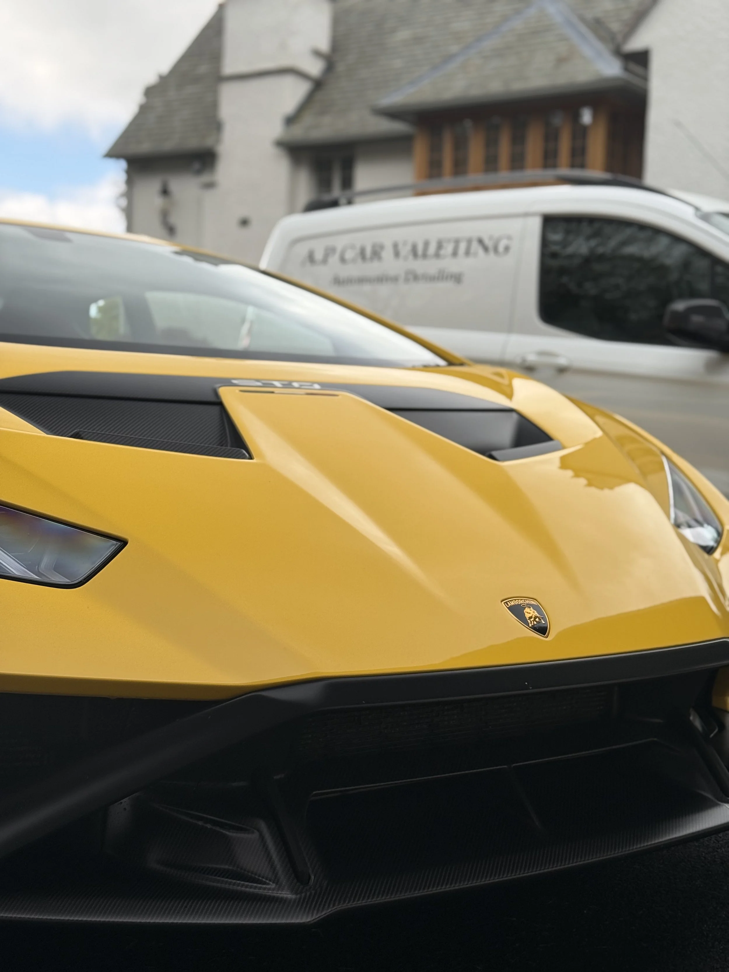 Close-up of a yellow Lamborghini sports car with the Lamborghini emblem on the front, parked outdoors.