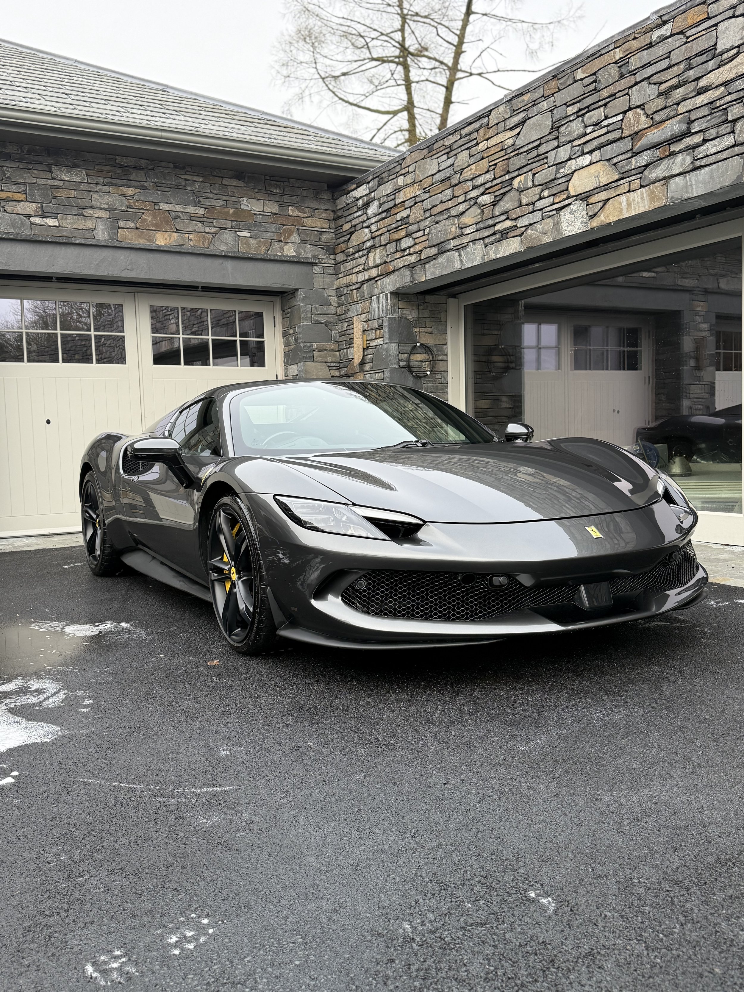 A silver sports car parked in a driveway in front of a stone house with garage doors.