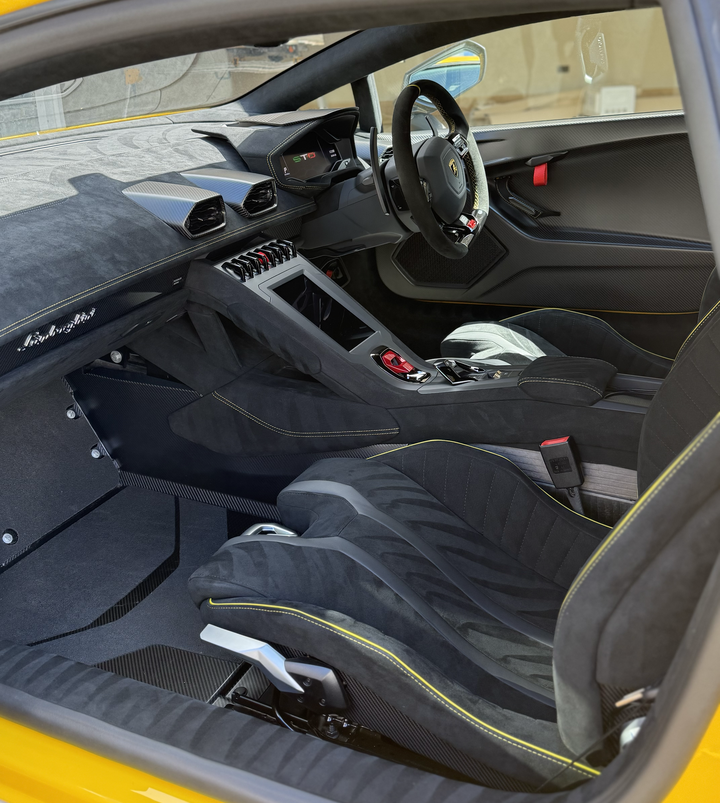 Interior of a yellow sports car showcasing a sleek dashboard with digital gauges, a racing steering wheel, carbon fiber accents, and black upholstery with yellow stitching.