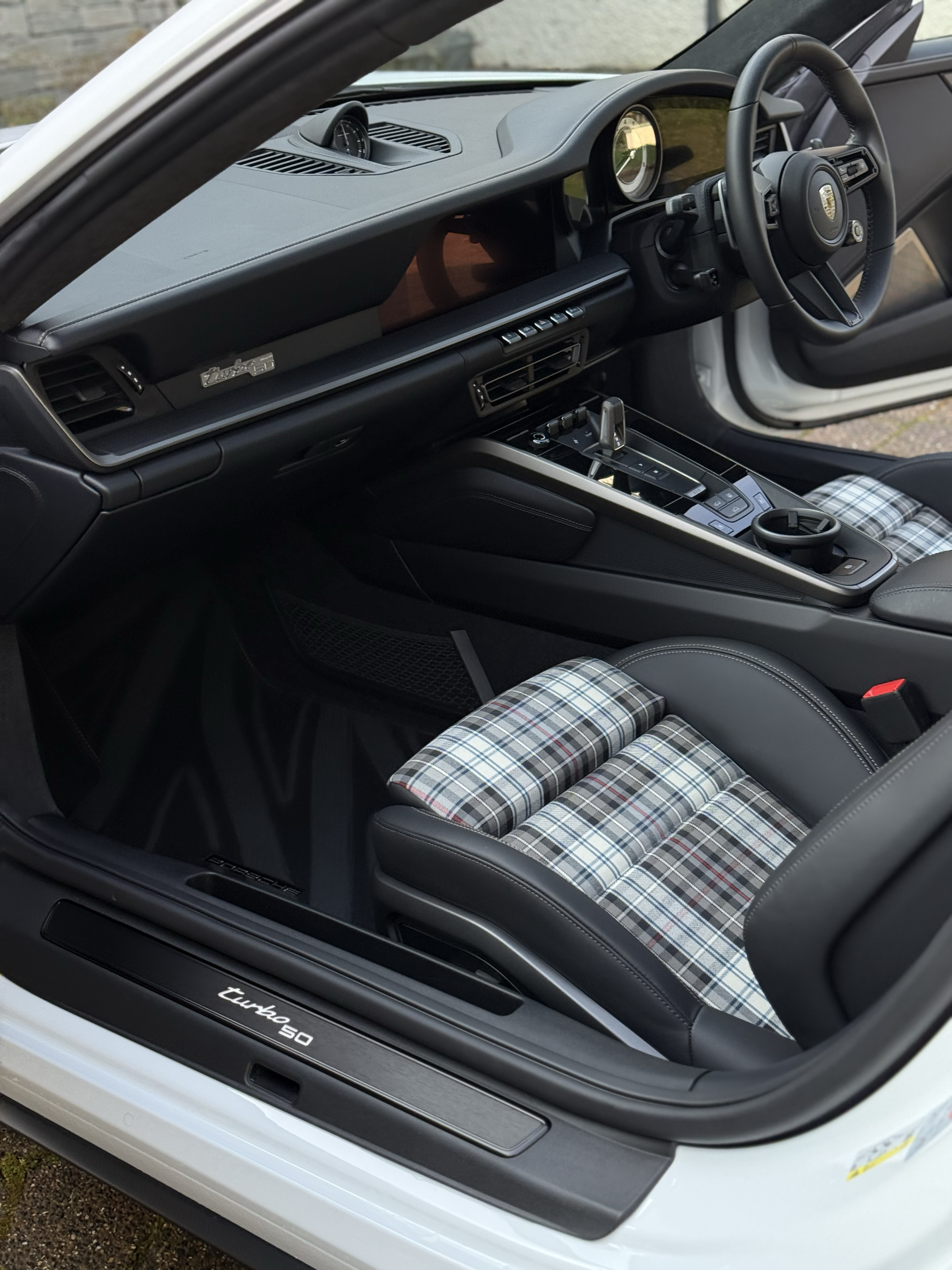Interior of a Porsche 911 Turbo S, showing the dashboard, steering wheel, gear shifter, and plaid-patterned seat.