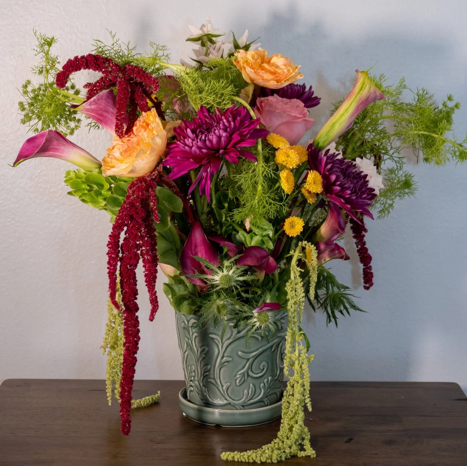 A tall ceramic vase with intricate floral patterns filled with a colorful mixed flower bouquet on a wooden surface.