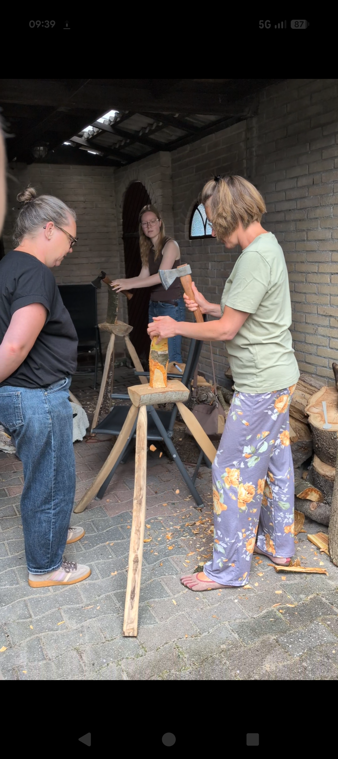 Mensen hakken hout met bijlen in een binnentuin of een soort buitenruimte, omringd door bakstenen muren.