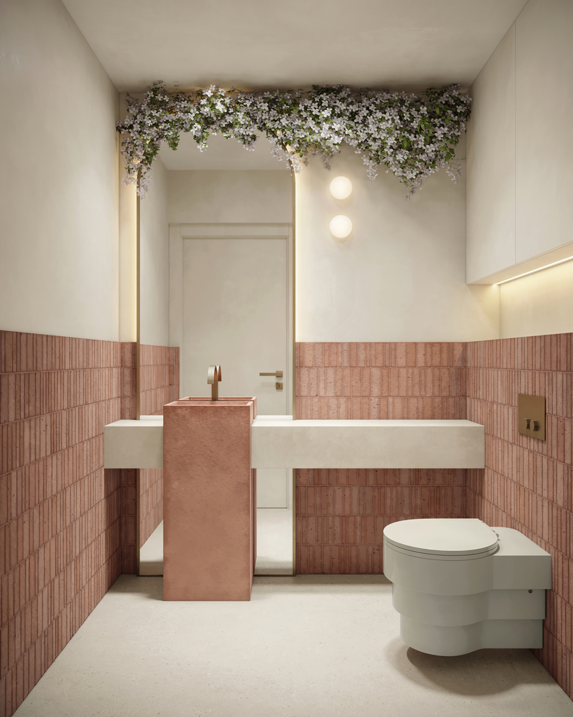 Petite salle de bain moderne avec un mur en briques rose, une cuvette de toilettes blanche, un lavabo en pierre rose, des fleurs blanches suspendues au plafond, et deux lampes rondes sur le mur.