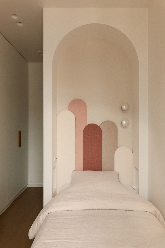 Lit simple dans une chambre au mur décoré avec des formes arrondies de différentes couleurs pastel.
