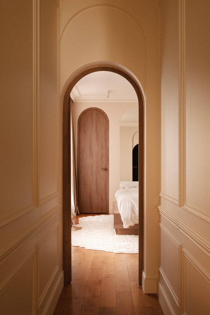 Une vue d'un couloir menant à une chambre avec un lit blanc, une porte en bois et un tapis blanc.