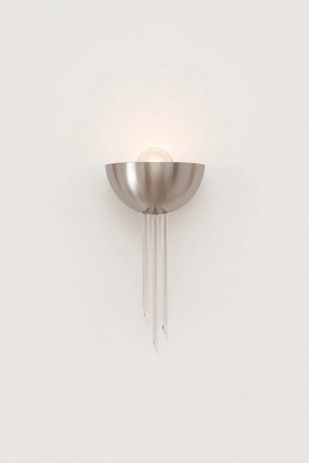 Applique murale en métal avec une ampoule apparente et des éléments en verre suspendus dessous, fixé à un mur blanc.
