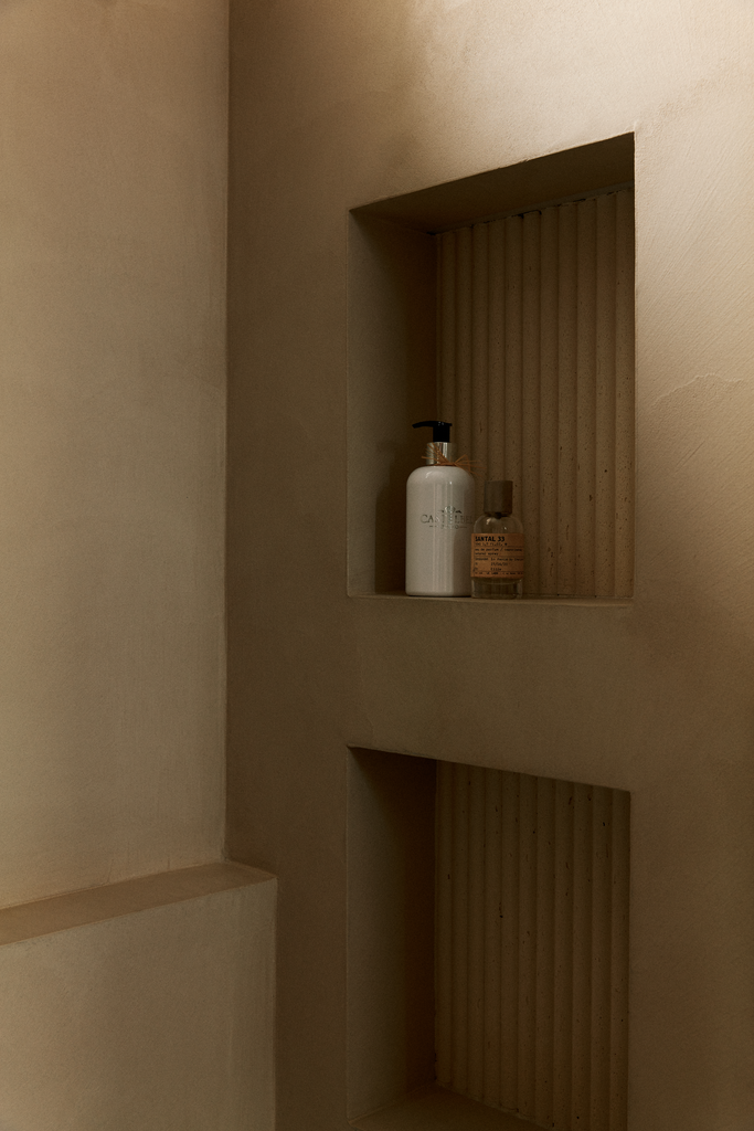 Une niche encastrée dans un mur, contenant une bouteille de savon ou lotion et une bouteille lifiée, probablement dans une salle de bain.