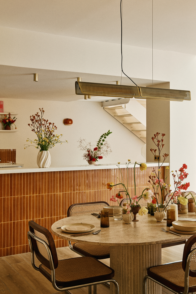 Salle à manger avec un grand bar en brique, table ronde en pierre avec vaisselle, verres et fleurs, décorée de vases avec des fleurs.