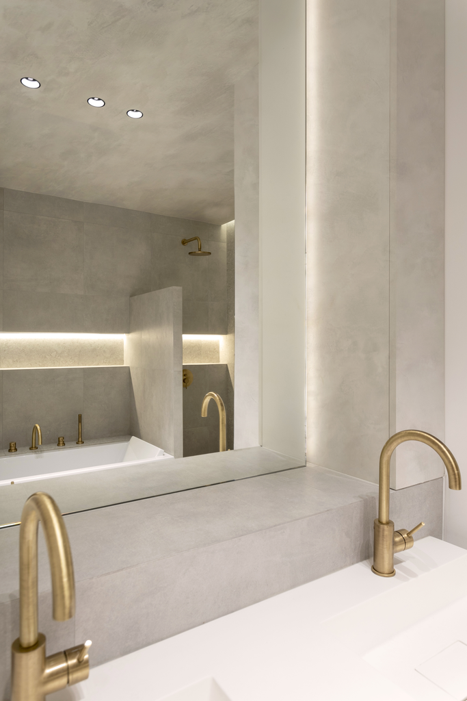 Vue d'un miroir dans une salle de bains moderne, reflétant une baignoire, un mur avec une douche, et des robinets en laiton.