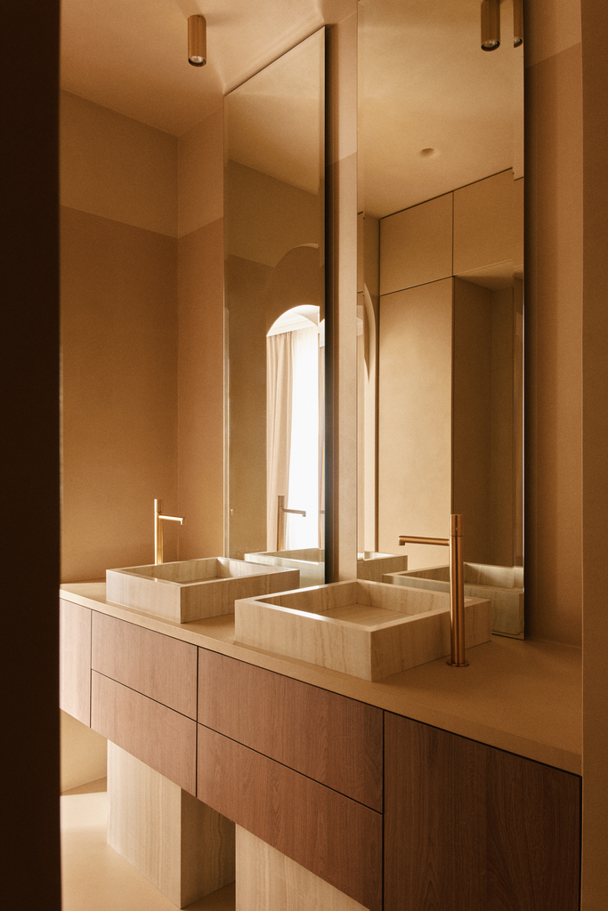 Lavabo moderne en pierre claire avec un miroir mural au-dessus dans une salle de bain élégante, éclairée par la lumière naturelle.