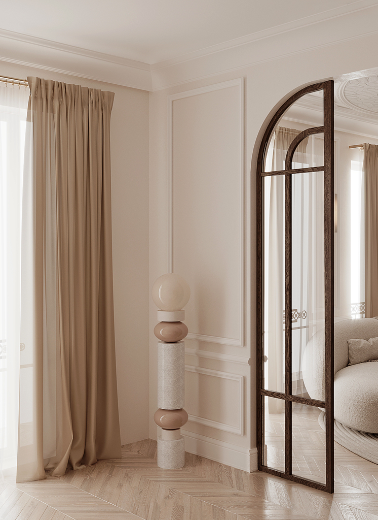 Intérieur d'une pièce élégante avec des rideaux beige, une lampe décorative en forme de sculpture avec plusieurs éléments en gris et beige, et une cloison en verre avec cadre en bois.