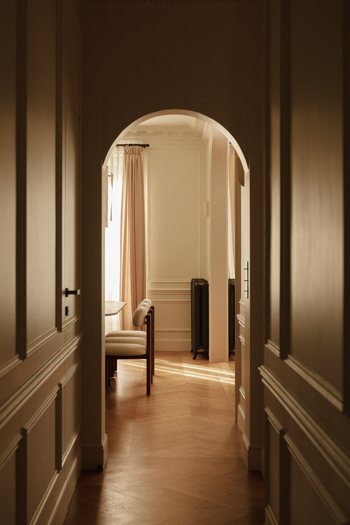 Vue d'un couloir menant à une pièce lumineuse avec un mobilier vintage et des rideaux beige.
