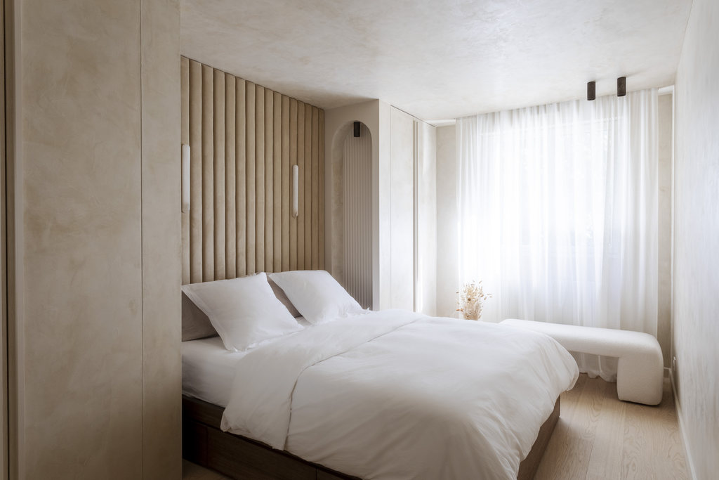 Chambre moderne avec lit blanc, murs clairs, grande fenêtre avec rideaux blancs, décoration minimaliste.