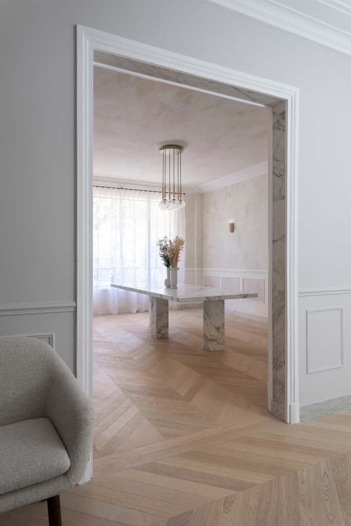 Intérieur d'une pièce lumineuse avec un meuble en marbre, un vase de fleurs, et un éclairage moderne, vue depuis un salon sur un espace salle à manger
