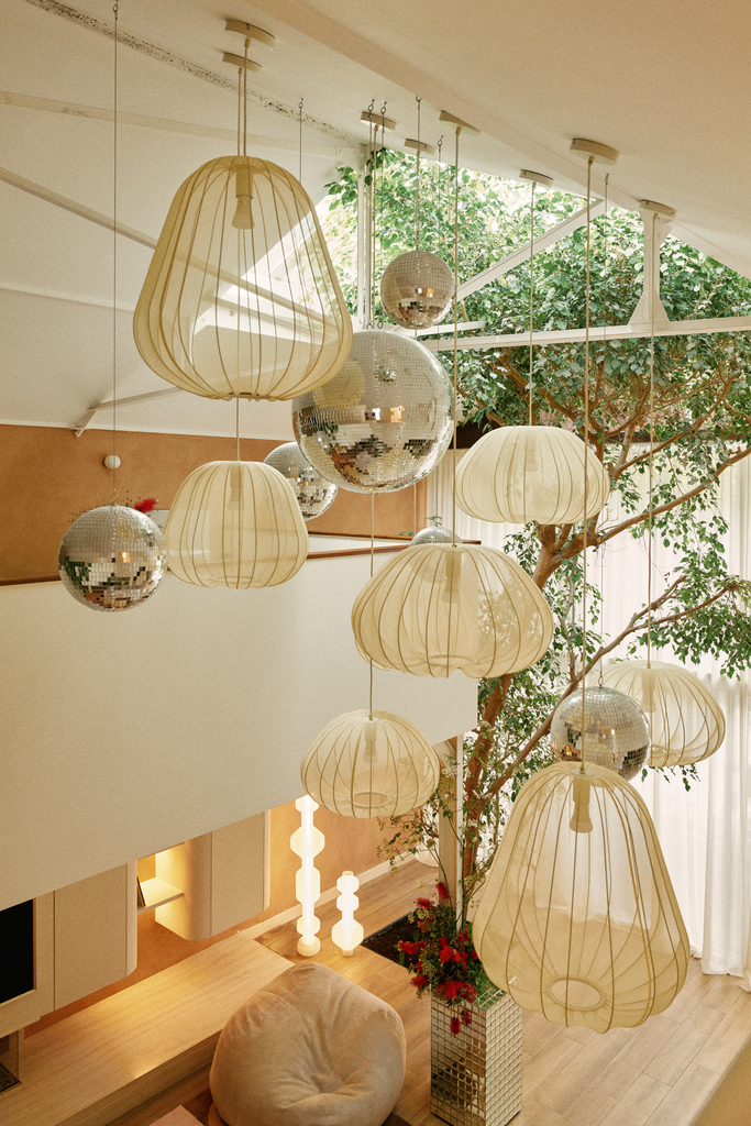 L'intérieur d'une maison avec un arbre en pot, plusieurs lampes suspendues allumées, dont des lampes en papier de style lanternes et des boules disco miroir, ainsi que des lumières au sol, créant une ambiance chaleureuse.
