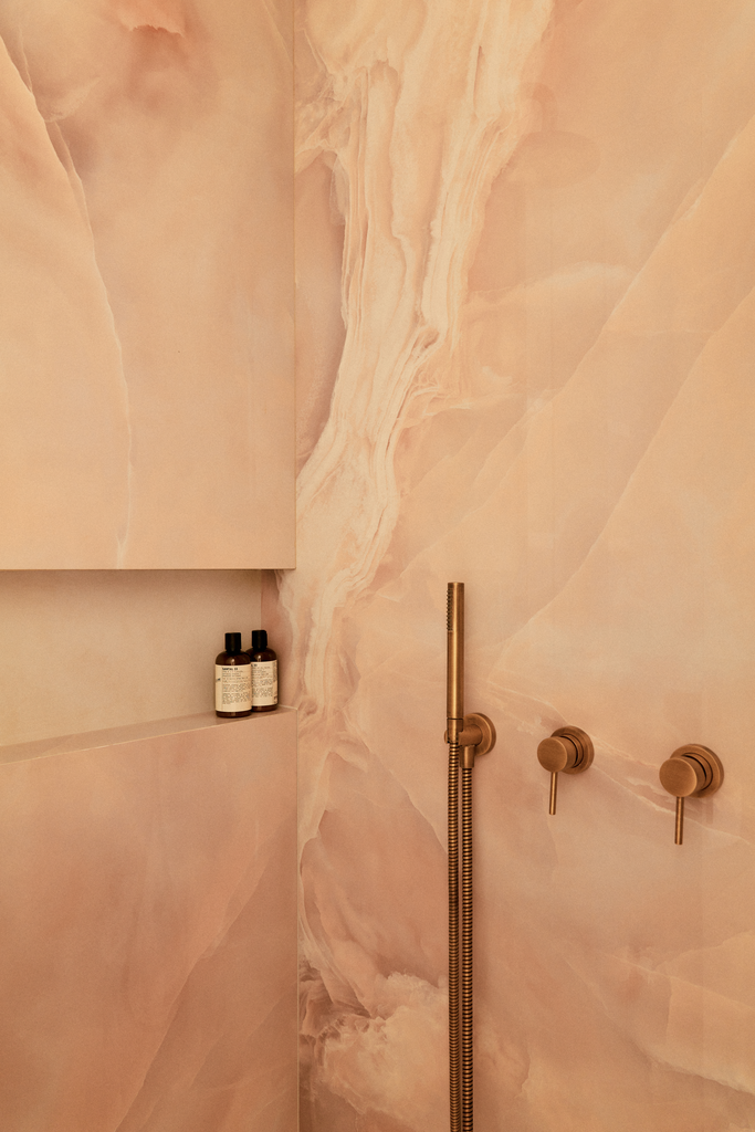 Intérieur d'une douche en marbre avec des bouteilles de produits de toilette noir et blanc posées sur une étagère.