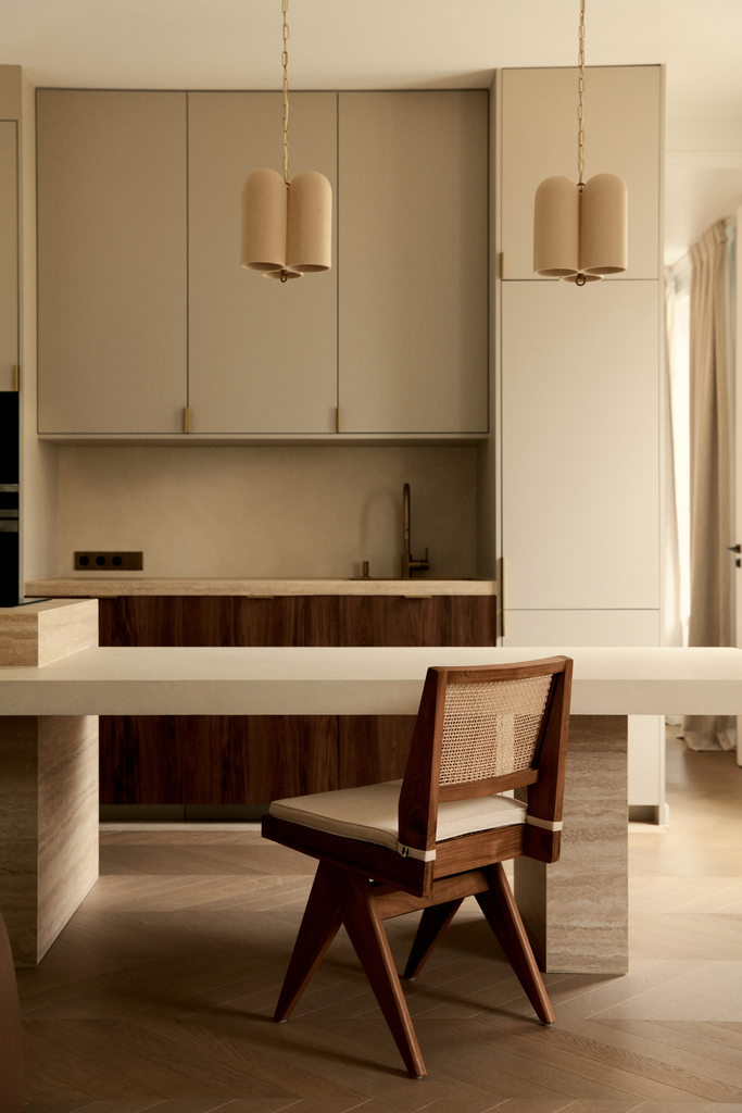 Une cuisine moderne avec des armoires blanches, un évier en acier inoxydable, un plan de travail en bois, et un fauteuil en bois avec un coussin, dans une ambiance chaleureuse.